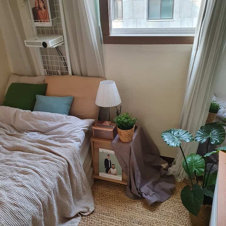 Bedroom in white, beige and wood tones featuring a nightstand, floor lamp, and plants, creating a cozy natural modern style.