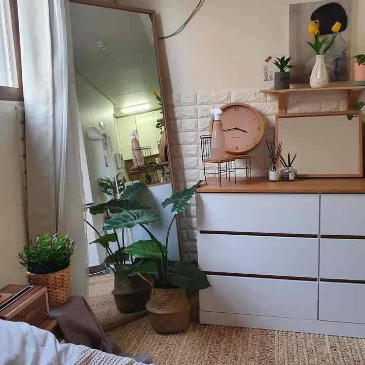 Natural-toned and white bedroom featuring a large mirror, clock, and plants arranged for a cozy atmosphere