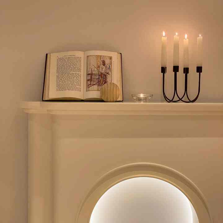 White-toned fireplace mantel featuring candles and open book in a cozy living room space