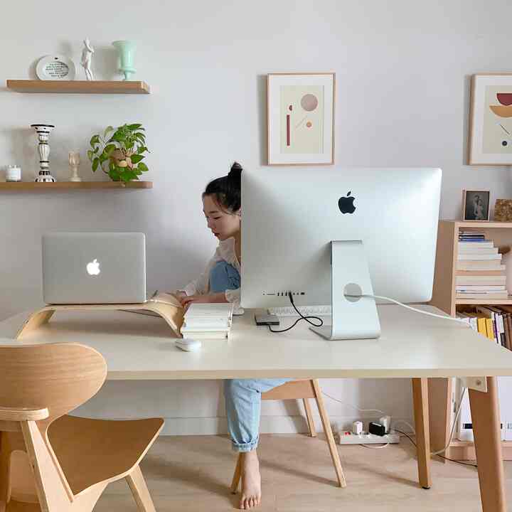 Bright white and wood tone study-style home office featuring a desk, large monitor, and a woman working in a clean workspace