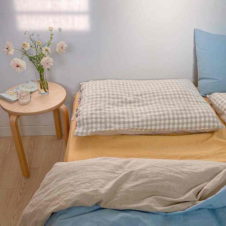 Bright beige and natural toned bedroom space featuring a wooden stool and checkered linen bedding creating a cozy atmosphere