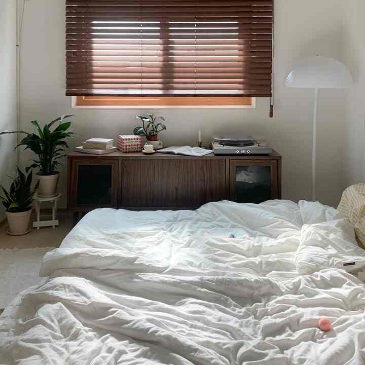白い寝具と木目調ブラインド、植物が配置されたナチュラルな雰囲気の寝室