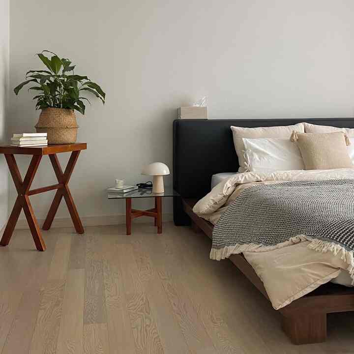 Natural tone bedroom featuring wood bed frame, nightstand, and plant with simple and cozy decor