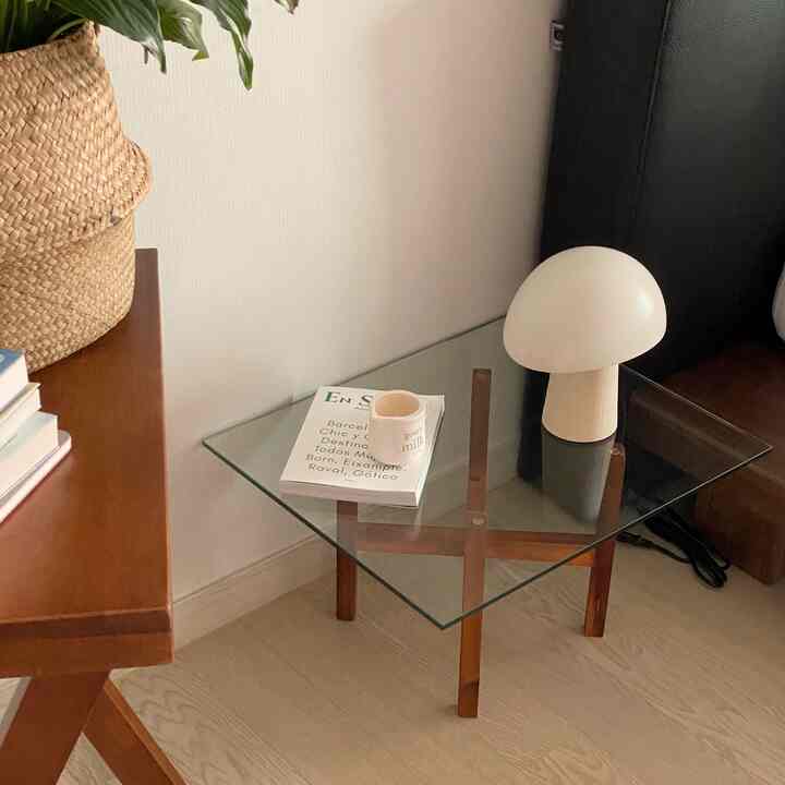 A living room with brown wood tones and white, featuring a glass nightstand topped with a table lamp and book, creating a natural atmosphere