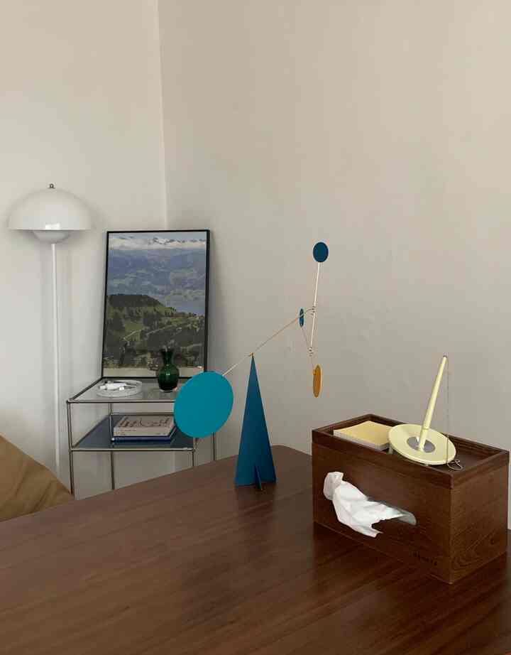 白い壁と木目調のテーブルが特徴のリビング、ブルーのモビールとトレイが置かれた落ち着いた雰囲気のインテリア