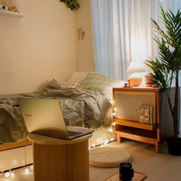 Beige-walled studio bedroom with wood-tone furniture, cozy lighting and cushions creating a warm atmosphere
