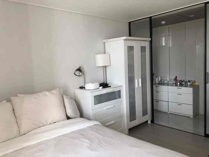 明るいホワイトトーンの寝室、中央に配置されたワードローブとチェストが清潔感とモダンな雰囲気を演出する空間