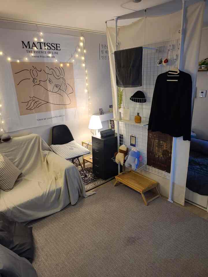 Natural color two-room apartment bedroom and living area featuring a beige sofa, rug, black nightstand, and ambient lighting in a cozy space