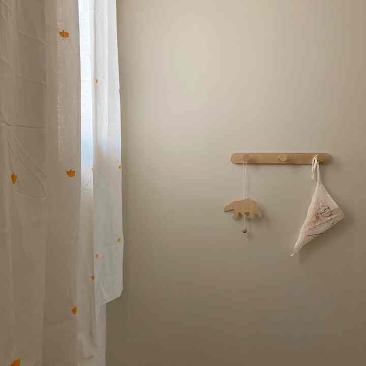 Beige-toned kids' room featuring orange-accented curtains and wooden wall hangers in a simple setting