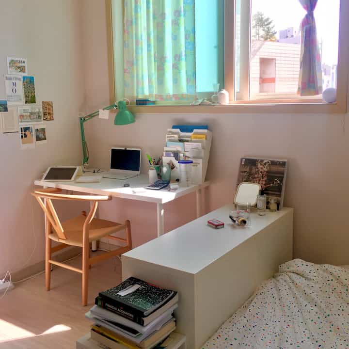 White and beige toned small bedroom with home office setup featuring desk, chair, and window with natural light