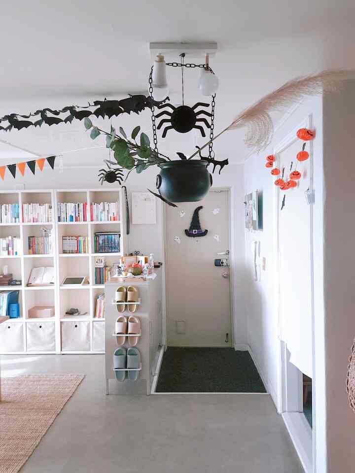 白い壁と広い玄関スペースにハロウィンの飾り付け、中央に吊るされた黒い魔女の鍋が配置された雰囲気のある空間