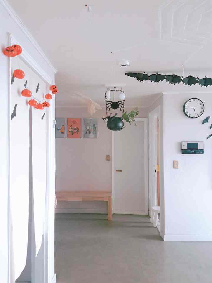 Bright white tone entrance space featuring white walls and ceiling, a wooden bench, and Halloween garlands creating a neat atmosphere