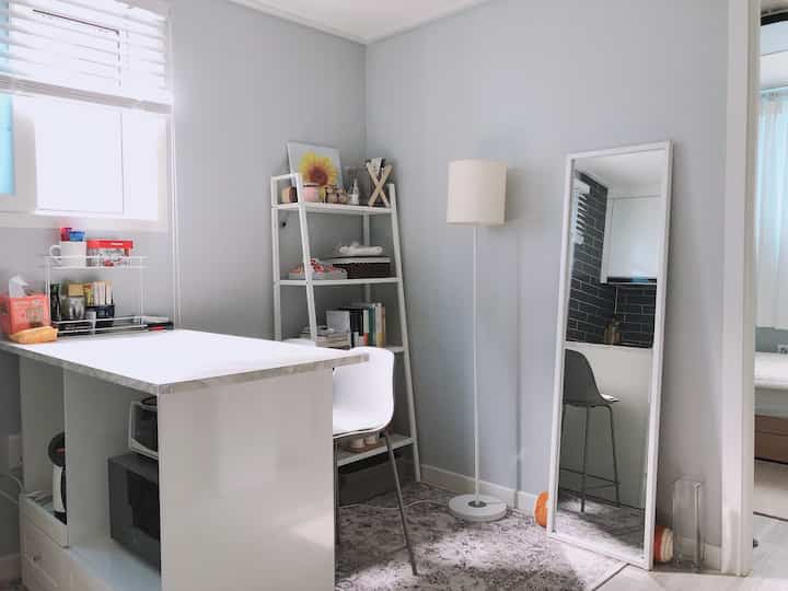 White-toned dining and kitchen space featuring a kitchen island, floor lamp, and full-length mirror with a modern, simple atmosphere