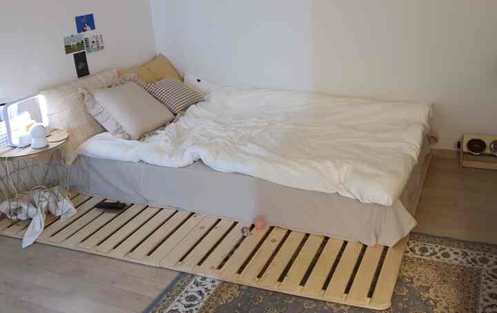 ナチュラルな木目調と白い掛け布団カバーが印象的なヴィンテージ寝室、快適なベッドとヴィンテージ風の枕が配置された雰囲気のあるインテリア