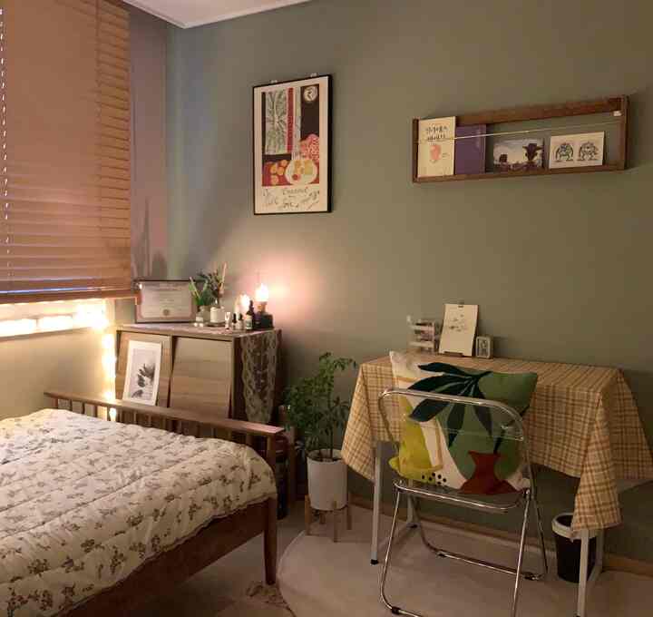 Natural brown and green toned bedroom featuring a wooden bed, folding desk, and transparent chair creating a cozy small room interior