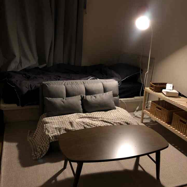 落ち着いたグレーと木目調の一人暮らしリビング、ソファベッドと小さな木製テーブル、ラタンバスケットが配置された雰囲気のあるインテリア