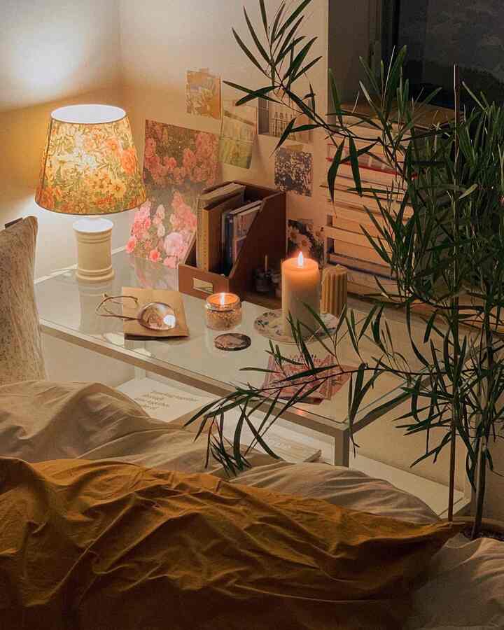 暖かいベージュとブラウンの色調の寝室、ヴィンテージ柄のランプが照らすデスクとキャンドル、植物が配された雰囲気のあるインテリア