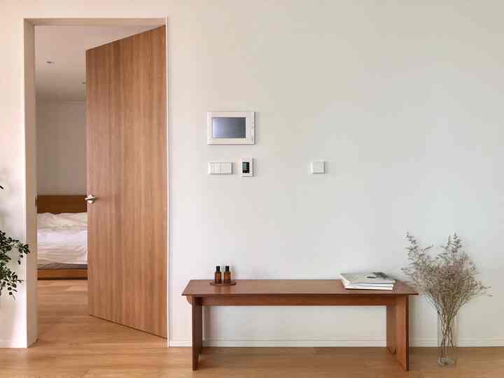 White walls and wood-tone floor featuring a wooden bench and dried flowers at cozy bedroom entrance interior
