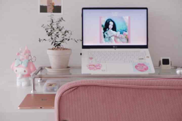 Studio apartment workspace with a pink chair and glass desk featuring a laptop and plant, creating a cozy atmosphere