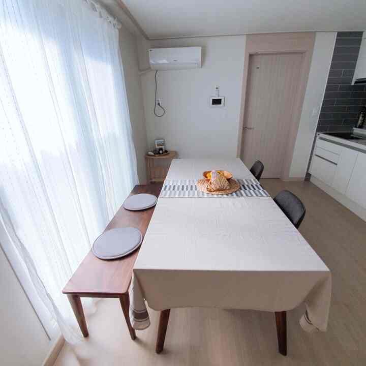 A white and wood-toned dining room featuring a bench by the window and a table with chairs, creating a clean natural atmosphere
