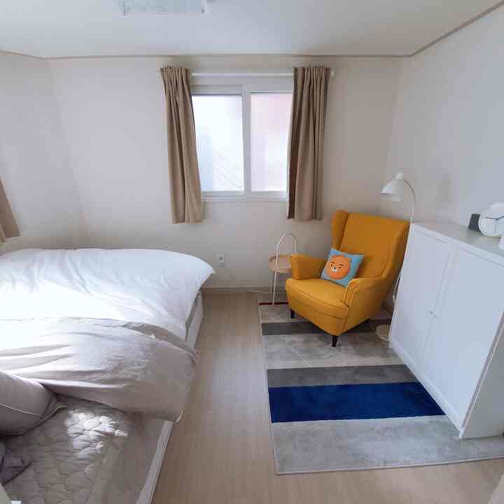 白とベージュのトーンの寝室、白いベッドと黄色のアームチェア、ベージュのカーテンが落ち着いたホテルライクな雰囲気の空間