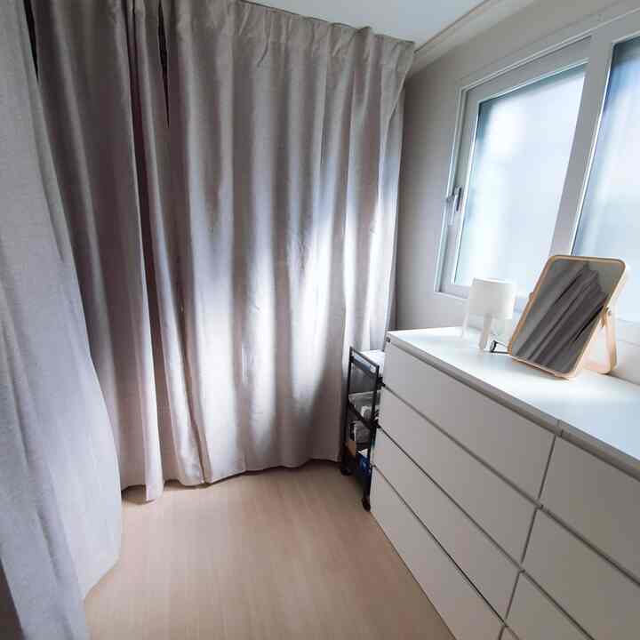 White and beige toned small room featuring long curtains, IKEA dresser, and fully enclosed wardrobe creating a neat space
