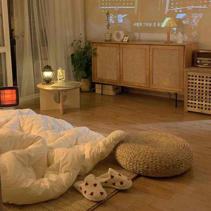 Natural wood tone floor with rattan furniture and white bedding, a cozy living room space featuring a mini projector displaying a movie