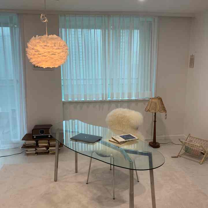 Simple modern home office space in white and beige tones featuring a glass desk and fluffy chair with minimalistic decor