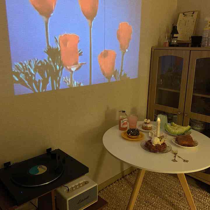 Beige and black toned home cafe space featuring a round table with desserts and a floral image projected on the wall by a projector, creating a cozy atmosphere