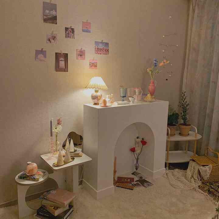 柔らかなベージュとホワイトの色調のリビングルーム、暖炉風オブジェ、多彩な花瓶、照明、モビールが配置された雰囲気のあるインテリア