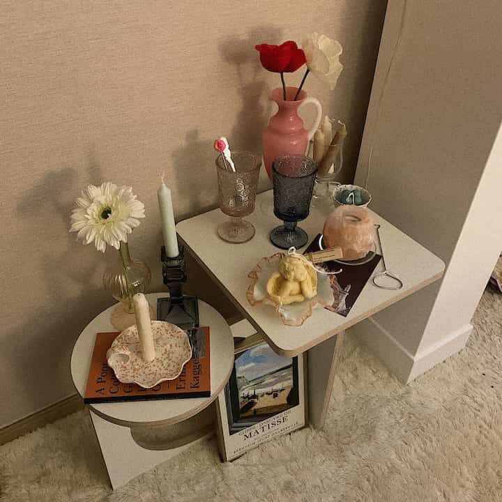 Warm beige-toned side table space with a rug, featuring vintage glassware and candles arranged neatly for a cozy home cafe vibe