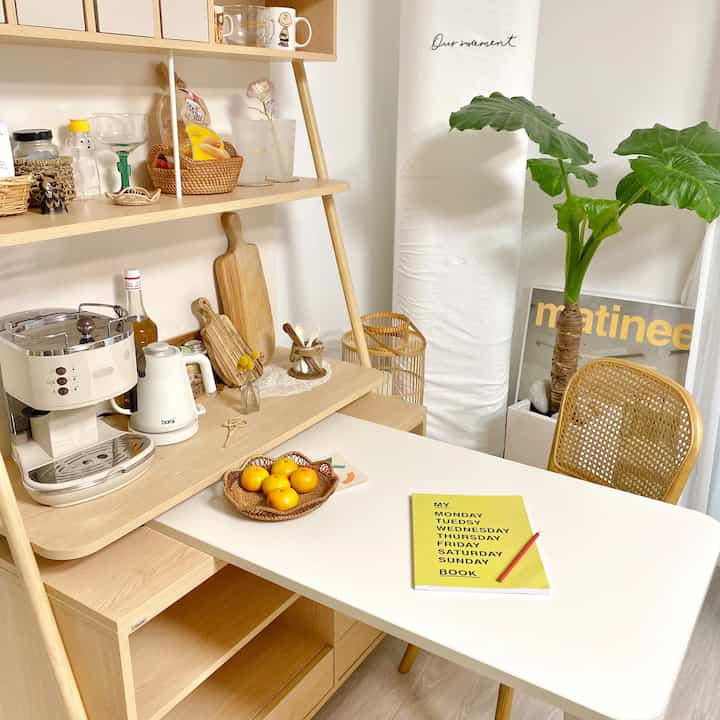 明るい白と木目調のキッチンスペース、ラタンチェアとコーヒーマシンが配置された雰囲気のあるおうちカフェ