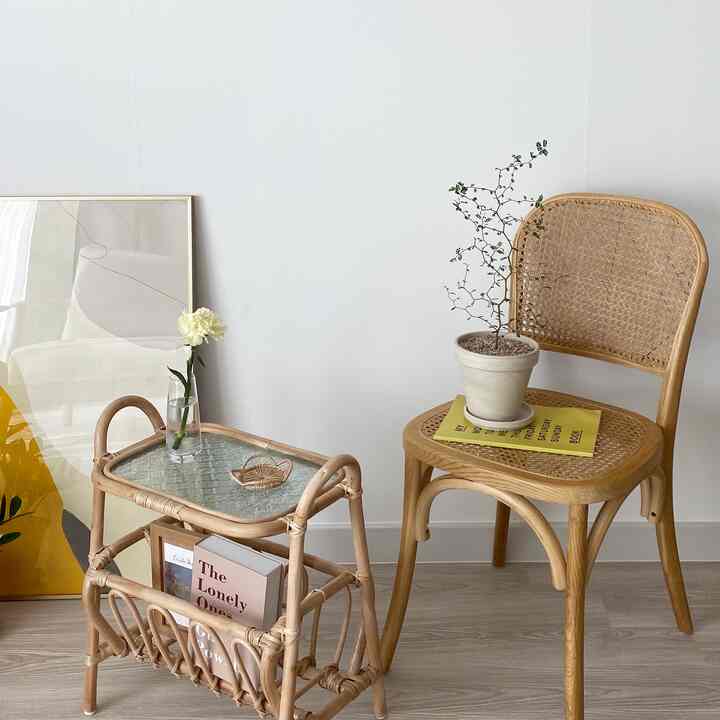 ナチュラルカラーのリビングコーナー、ラタンチェアとラタン製サイドテーブル、鉢植えとシンプルな額縁が配置された雰囲気のあるインテリア