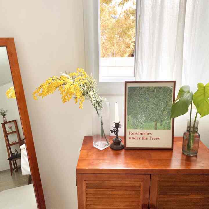 ナチュラルなブラウン調の寝室、木製キャビネットに額縁と花、鏡が配置された落ち着いたインテリア