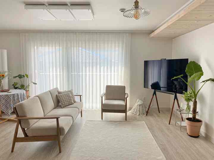 Bright white and wood-toned living room featuring beige sofa and armchair, rug, and easel-style TV stand creating a cozy atmosphere