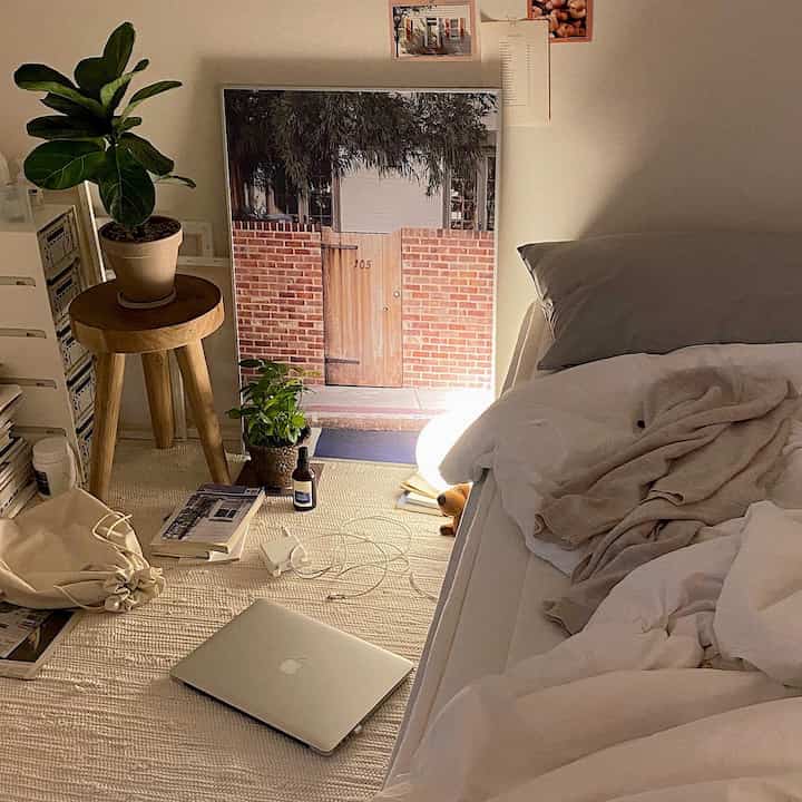 Natural beige and white toned bedroom featuring wooden stool with plants and a poster, creating a cozy atmosphere