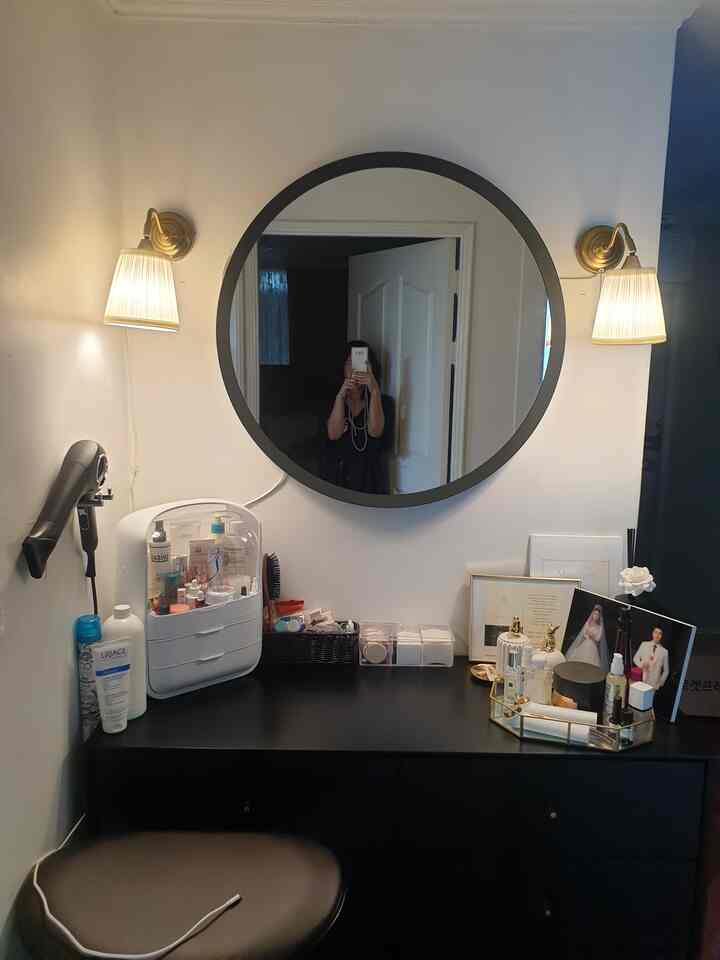 Powder room with black vanity desk and large round mirror, white walls and gold wall lamps creating a warm atmosphere