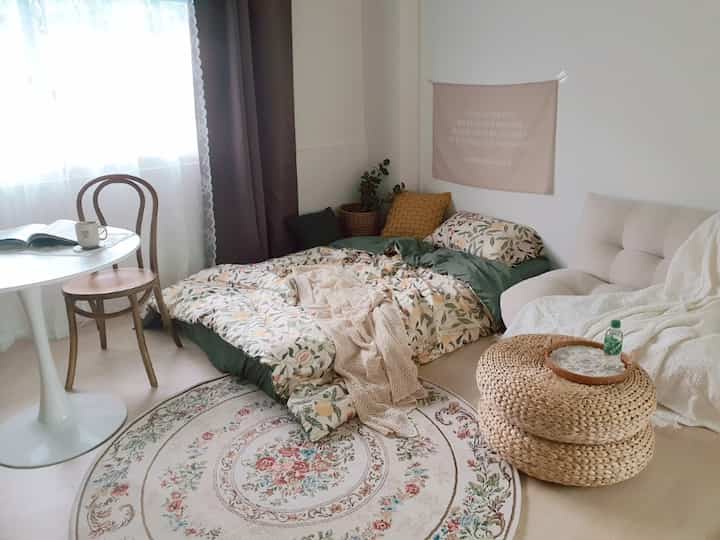 Light beige natural wood tone bedroom featuring autumn-themed orange and green bedding with a rattan stool in a cozy setting