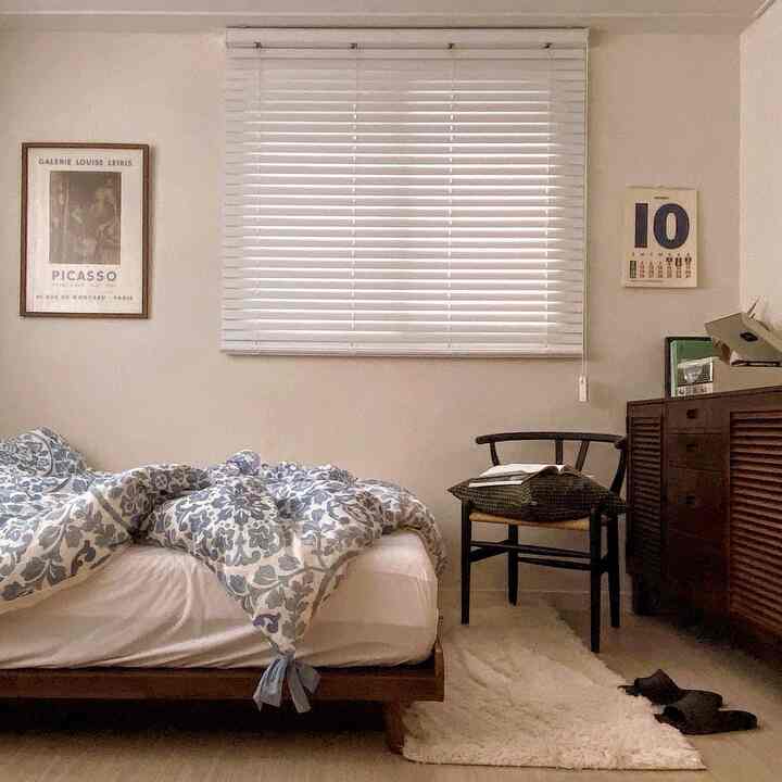 ベージュの壁と木目調家具、白いブラインドが配置されたシンプルでナチュラルな寝室のインテリア
