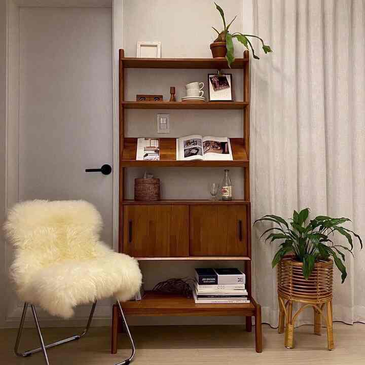 A cozy small room featuring natural wood tones and rattan plants, with a white armchair and curtains harmoniously arranged
