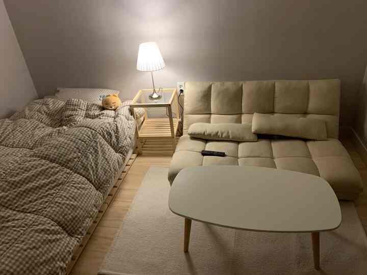 木目調とベージュのワンルームリビング、ベッドとソファ、ナイトランプが配置された雰囲気のあるインテリア。