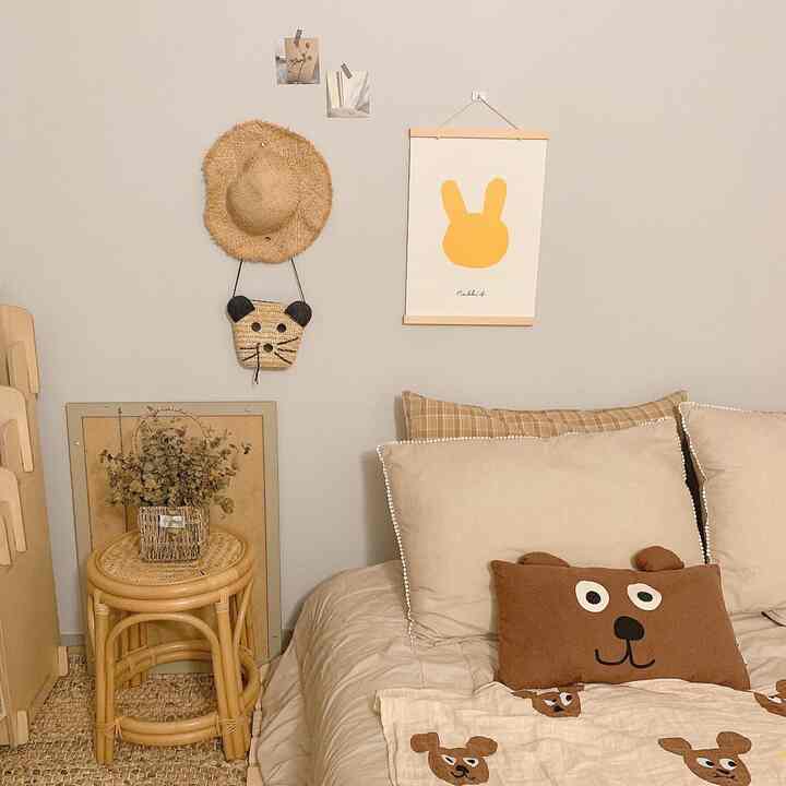 ベージュとナチュラルトーンの寝室、ラタンのスツールと赤ちゃん用寝具が配置された雰囲気のあるインテリア