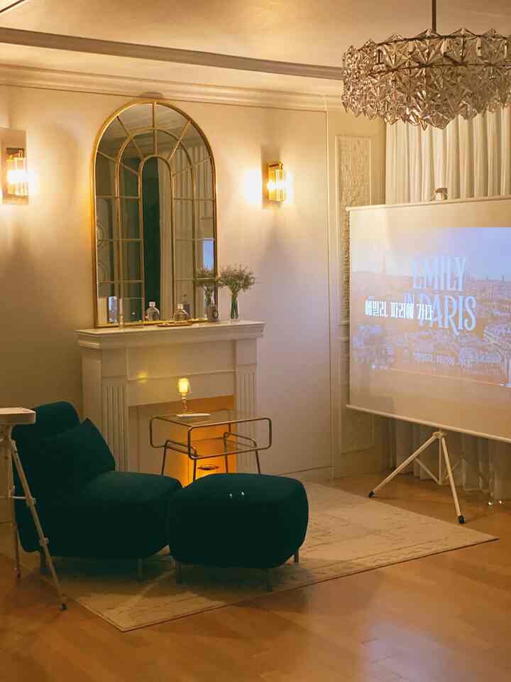 Natural warm-toned living room featuring deep green armchair, gold side table, and projector screen in a cozy home cinema setting