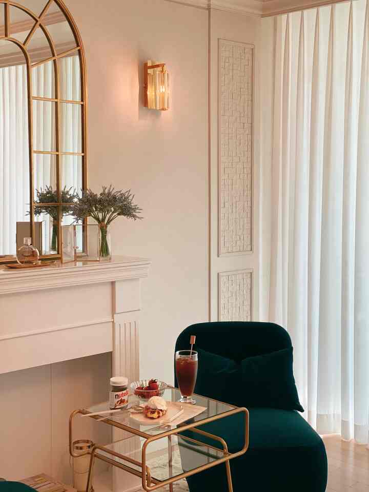 Cozy winter mood living room featuring a dark green armchair, transparent gold-framed side table, lavender decor, and warm wall sconces