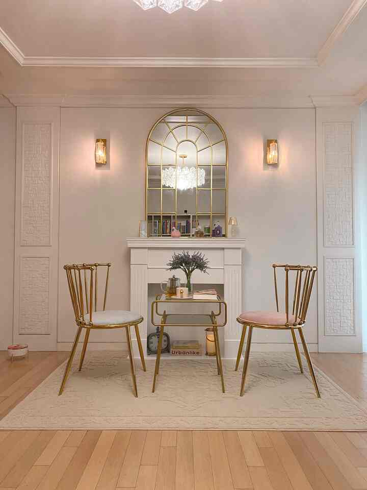 ゴールドとナチュラルカラーのリビング、金属製サイドテーブルと壁照明が配置されたカフェ風の雰囲気あるインテリア