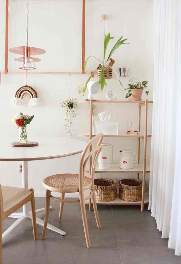 Bright and natural dining room with white walls and wood tones, featuring a wooden dining table, chairs, shelf with plants and decor for a cozy vibe