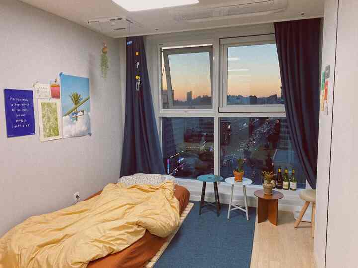 A small bedroom for single household featuring blue curtains and beige wood flooring with an urban city view through the window