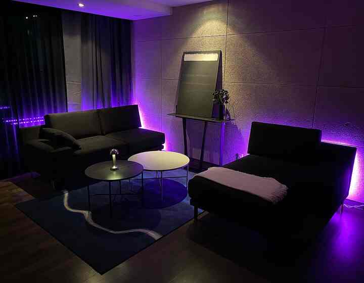 Modern living room with purple LED lighting, featuring black sofas and round coffee tables in a cozy setup