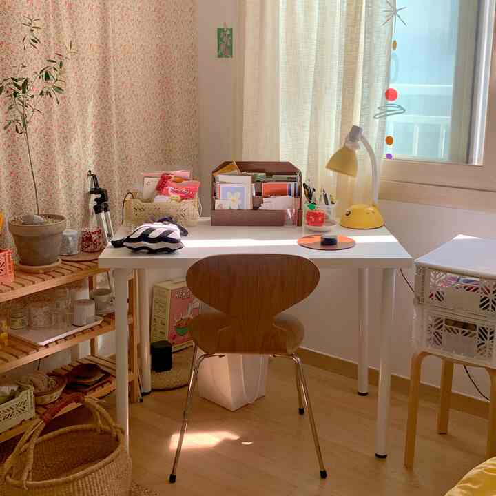 Small white and wood tone workspace featuring a white desk, yellow desk lamp, and organized storage in a cozy room