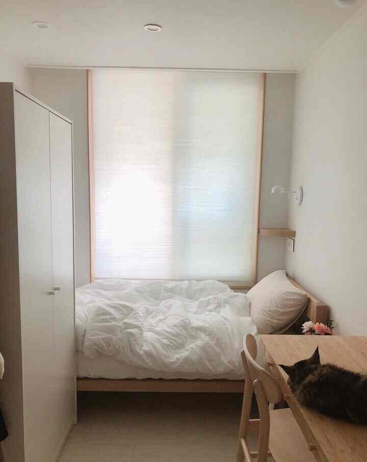 A clean bedroom in white and wood tones, featuring a bed and desk arranged in a natural modern style